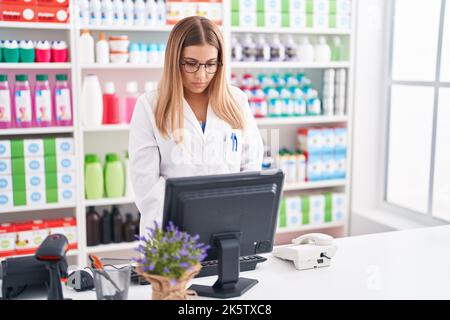Junge schöne hispanische Frau Apothekerin mit Computer in der Apotheke Stockfoto