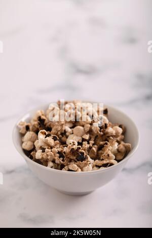 In der kleinen weißen Schüssel auf grauer Keramik verbranntes Popcorn Stockfoto