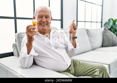 Älterer Mann hält Pillen mit einem großen Lächeln im Gesicht und zeigt mit dem Finger auf die Seite, die auf die Kamera schaut. Stockfoto