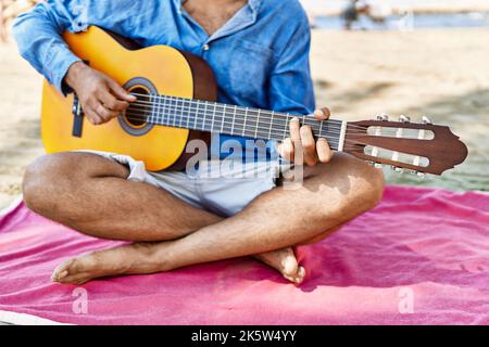 Mann, der klassische Gitarre spielt, sitzt auf Sand am Strand. Stockfoto