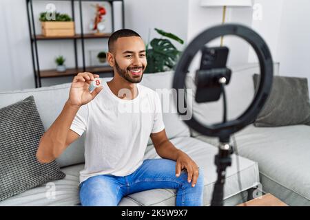 afroamerikanischer Mann, der vlog Tutorial über Bitcoin aufzeichnet, mit dem Smartphone zu Hause, das positiv und glücklich steht und mit einem selbstbewussten SM lächelt Stockfoto