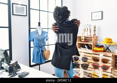 Afrikanische junge Frau, die als Managerin in der Einzelhandelsboutique arbeitet und sich glücklich und positiv von hinten umarmt Stockfoto