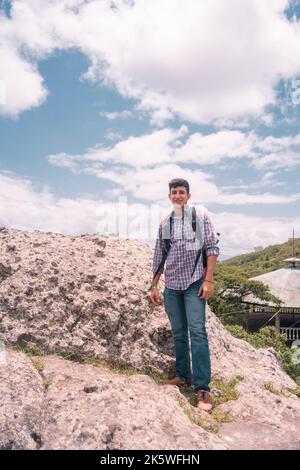 Ein lateinischer Teenager auf einem Felsen, der lächelt und in die Kamera schaut Stockfoto