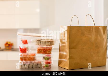 Sushi-Rollen in einer Plastikbox neben einem Papierpaket auf einem weißen Tisch. Lieferung. Mitnehmen. Stockfoto