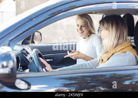 Porträt von zwei jungen glücklich attraktiven Frauen Freunde Schwestern sitzen im Auto. Der Fahrer setzt die Hände auf das Lenkrad. Stockfoto