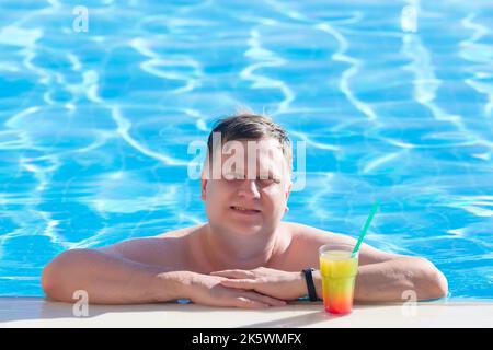 Mann, der einen Cocktail genießt, während er im Pool schwimmend. Stockfoto