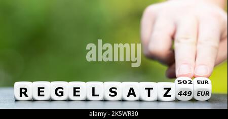 Die Hand dreht Würfel und ändert den deutschen Ausdruck 'Regelsatz 449 Euro' in 'Regelsatz 502 Euro'. Symbol für die Erhöhung von Stockfoto