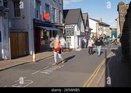 Menschen Frau, die im Herbst auf der Straße läuft und die Buchhandlung am National Bookshop Day in der Buchstadt Hay-on-Wye Powys Wales UK KATHY DEWITT abschreibt Stockfoto