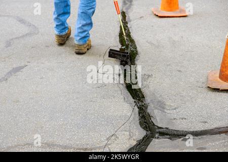 Ein asphaltischer Fugenriss muss bei Restaurierungsarbeiten auf der Asphaltstraßenoberfläche abgedichtet werden Stockfoto