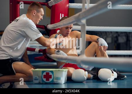 Persönlicher Trainer, Teamtrainer, der männlichen Boxer hilft, die Hand zu entspannen, vermeiden Sie Verletzungen während des Boxtrainings im Fitnessstudio Stockfoto