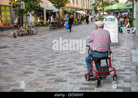 Älterer Mann, der auf einem Roller oder Gehhilfe in der Fußgängerzone ISO Roobertinkatu im Stadtteil Punavuori in Helsinki, Finnland sitzt Stockfoto