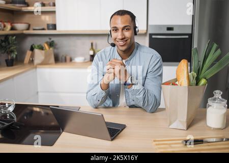 Porträt eines arabischen Geschäftsmanns, der während der Arbeit von zu Hause aus gesunden Salat zubereitet. Attraktive gut aussehende Männer fühlen sich glücklich, Laptop-Computer-Studie, lernen online, bevor sie sauberes Gemüse in der Küche zu essen. Stockfoto