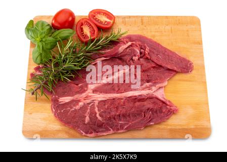 Rohes Rindersteak auf Holzschneidebrett mit Basilikum-, Rosmarin- und Kirschtomaten isoliert auf weißem Dolly Shot Stockfoto