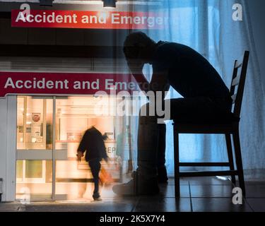 NHS Krankenhaus Unfall- und Notaufnahme mit Bild eines Mannes mit Kopf in den Händen. Überarbeiteter Arzt, Stress, psychische Gesundheit, Ärzte... Konzept. Stockfoto