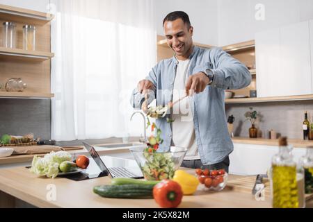 Konzentrieren Sie sich auf die Hände von Menschen, die Holzlöffel halten und Zutaten in einer Glasschüssel mischen, und bereiten Sie auf der modernen Kücheninsel ein köstliches, gesundes Frühstück oder Abendessen zu. Stockfoto