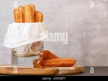 Churros mit Zucker und Karamellsauce in einem grauen Glastisch mit Kopierraum Stockfoto