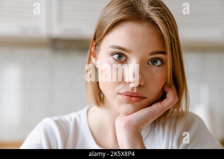 Nahaufnahme einer jungen weißen blonden Frau im Innenbereich, die die Kamera auf der Hand ansieht Stockfoto