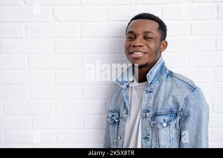 Portrait junger hübscher afrikanischer schwarzer Mann, der Jeansjacke an Backstein trägt und im Freien eine Wand mit Copyspace hat. Stockfoto