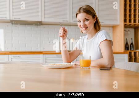 Lächelnde junge Frau, die zu Hause in der Küche ein gesundes Frühstück serviert Stockfoto