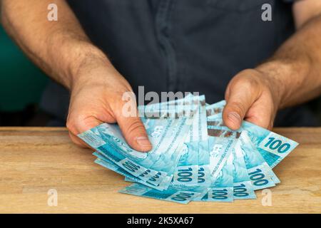 Der Mann hinter dem Schreibtisch hält ein Paket von hundert reais brasilianischen Rechnungen Stockfoto