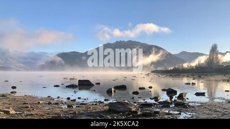 Ein tiefes Alaska-Panorama mit dem See voller Steine und Nebel, Bergen und Himmel Hintergrund Stockfoto