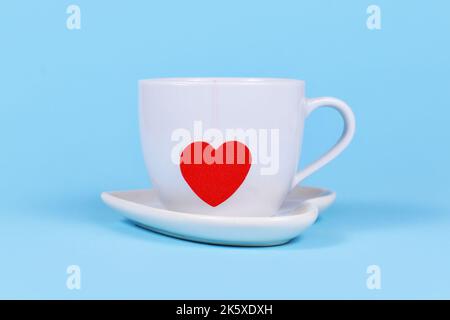 Weiße Teetasse mit rotem herzförmigem Teebeutelpapier auf blauem Hintergrund Stockfoto