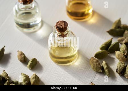 Eine Flasche ätherisches Aromatherapie-Öl mit Kardamom-Samen auf weißem Hintergrund Stockfoto