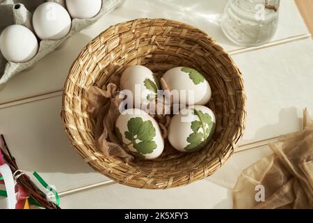 Rohe Ostereier mit Kräutern, die an ihnen befestigt sind, bereit, mit Zwiebelschalen gefärbt zu werden, in einem Korb Stockfoto