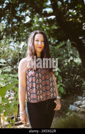 Schöne junge glückliche Mischling japanische Frau in Jeans und Hemd im Sommerpark, lächelnd Stockfoto