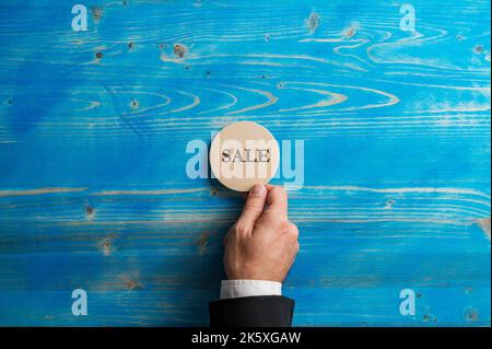 Hand eines Geschäftsmannes, der einen Kreis aus Holz mit dem Wort Sale Cut auf blauem Hintergrund platziert. Stockfoto