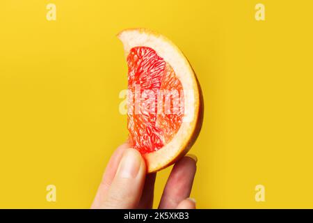 Defokussieren Sie die weibliche Hand mit einem Stück einer roten Grapefruit. Gesundes Lebensmittelkonzept. Frischer Orangensaft. Veganes, vegetarisches Konzept. Banner mit Kopierbereich. Ci Stockfoto