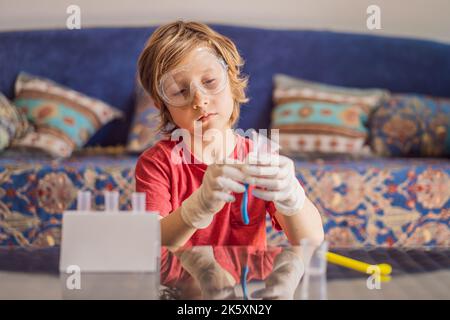 Kind Junge tun chemische Experiment zu Hause. Kinder mit Schutzbrille untersuchen Pipettentropfflüssigkeit in Reagenzgläser, Kaukasisch und Biochemie Stockfoto