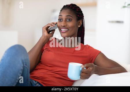 Schöne Schwarze Frau Im Gespräch Auf Handy Und Kaffee Zu Hause Trinken Stockfoto