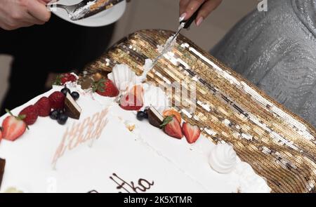 Schneiden Sie einen Geburtstagskuchen. Der Kuchen in Nahaufnahme. Messer in der Hand einer Frau. Stockfoto