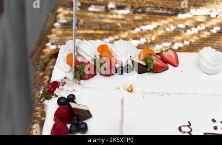 Schneiden Sie einen Geburtstagskuchen. Der Kuchen in Nahaufnahme. Messer in der Hand einer Frau. Stockfoto