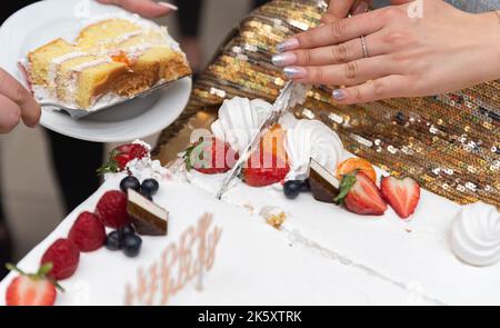 Schneiden Sie einen Geburtstagskuchen. Der Kuchen in Nahaufnahme. Messer in der Hand einer Frau. Stockfoto