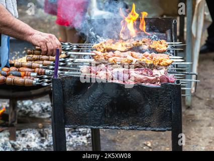 Gegrilltes appetitliches Kebab-Kochen auf Metallspießen. Shashlik während des Kochens auf dem mangal über heißen Kohlen im Freien, Street Food. Saftige Stücke Stockfoto