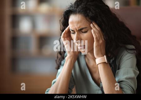 Verärgerte junge Frau, die während der Arbeit an Kopfschmerzen leidet Stockfoto