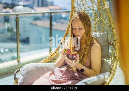 Portrait einer wunderschönen Frau in einem wunderschönen Kleid, die auf einer Terrasse sitzt und Erdbeere isst Stockfoto