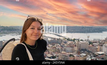 Junge Touristenfrau bei Sonnenuntergang mit der Istanbuler Landschaft. Junge, schöne Frau, die Istanbul vom Galata-Turm aus beobachtet. Stockfoto