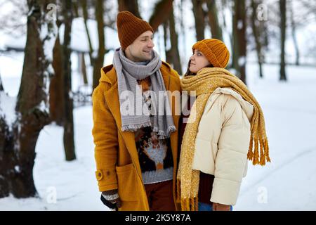 Waist-up-Porträt eines glücklichen Paares, das sich im Winterwald ansieht, während Sie in der Natur spazieren gehen Stockfoto