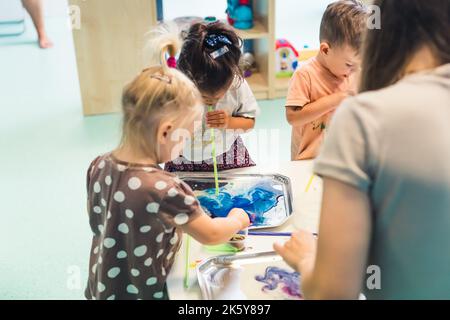 Kinder, die in die kleinen Tuben blasen, um im Kinderzimmer mit Aquarellen zu malen, Konzept für mittelgroße Vorschulkinder. Hochwertige Fotos Stockfoto