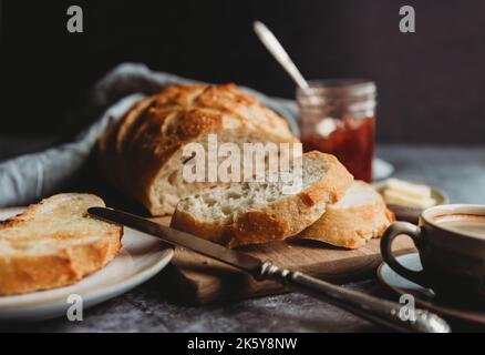 Nahaufnahme von geschnittenem Brot mit Butter, Marmelade und Kaffee. Stockfoto