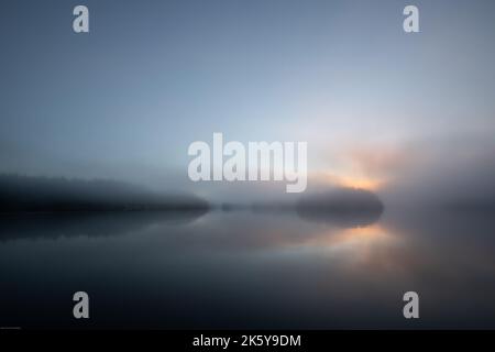 Morgennebel mit Sonne, die durch Wolken und Spiegelungen im Hafen, Blunden Harbour, British Columbia, Kanada, guckt. Nebel auf einem Hafen Stockfoto