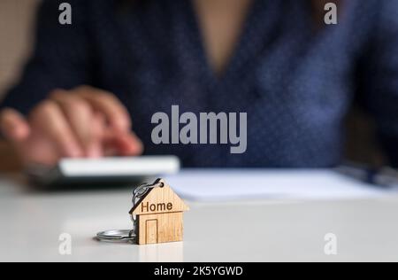 Home Schlüsselanhänger mit Frau auf Rechner im Hintergrund. Immobilienbewertung oder Anlagekonzept. Stockfoto