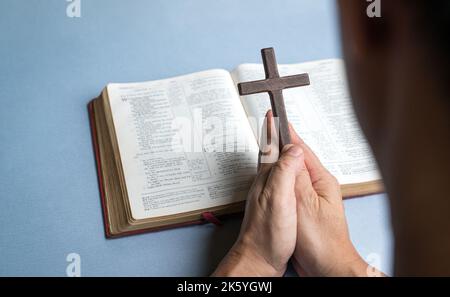 Mann, der im Hintergrund die Kreuzkreuzifx mit der offenen bibel hält. Christliches Glaubenskonzept. Stockfoto