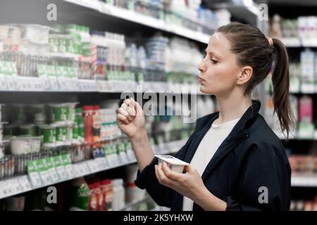 Eine Frau wählt Joghurt in einem Geschäft. Nützliche Lebensmittel Theke Auswahl Kauf Käufer. Stockfoto