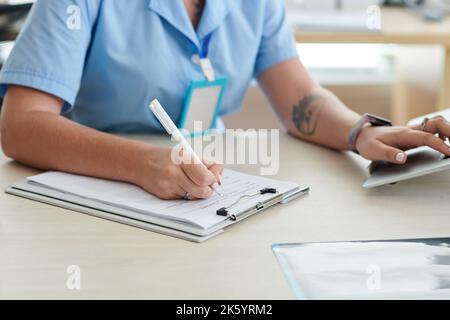 Nahaufnahme einer Ärztin, die am Tisch im Büro sitzt und die Patientenkarte füllt Stockfoto