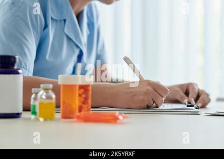 Nahaufnahme einer jungen Krankenschwester, die dem Patienten Medikamente verordnet, während sie mit Pillen am Tisch sitzt Stockfoto