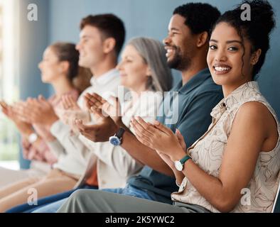 Eine Gruppe von fröhlichen Geschäftsleuten klatscht, während sie in einer Reihe bei einem Treffen zusammen sitzen. Porträt einer jungen Geschäftsfrau mit gemischter Rasse, die klatscht Stockfoto